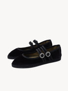 Black velvet shoes with decorative straps on a light background