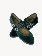Pair of green velvet shoes with decorative straps on a light background