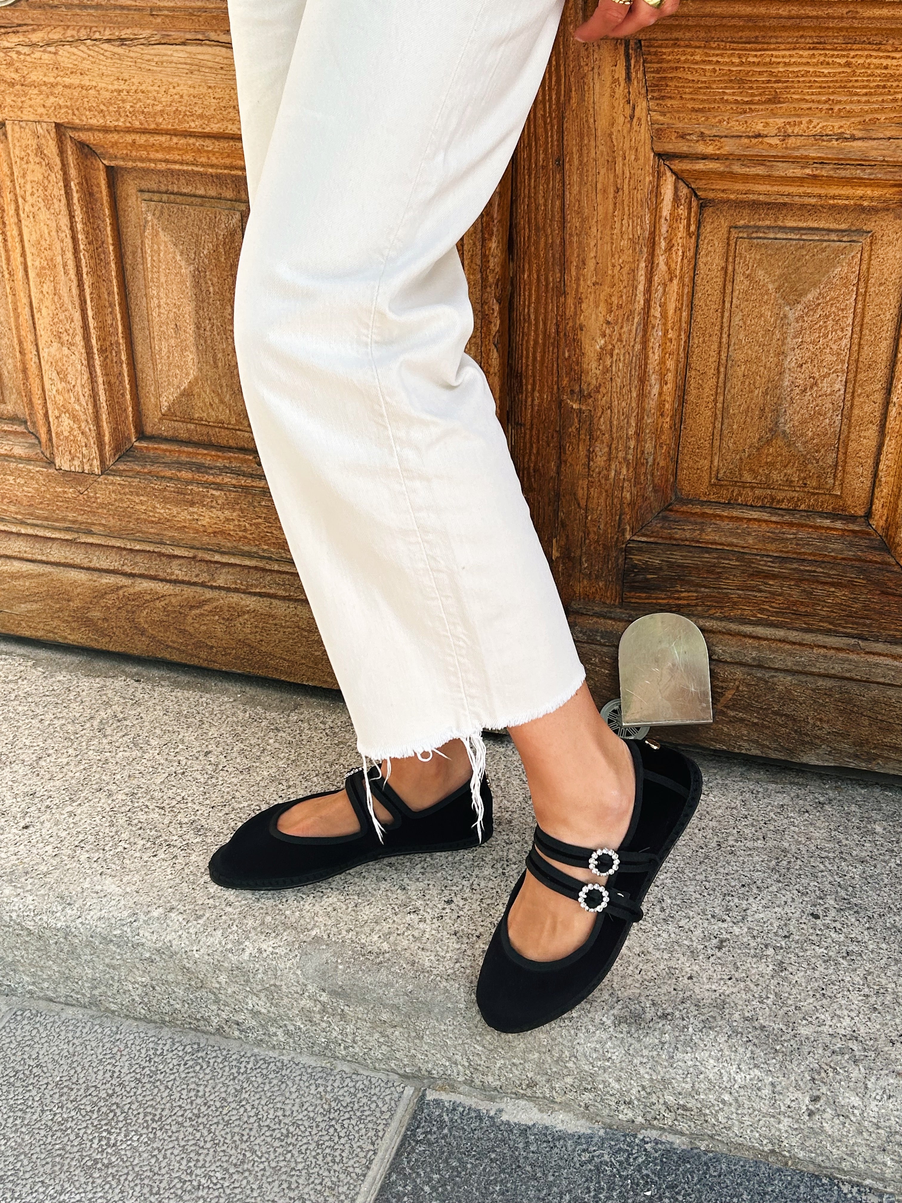 Person wearing black flats with white pants stepping onto a stone surface.