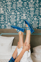 Person wearing blue sandals with floral patterns on a bed with decorative headboard.