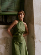 Woman in a green dress leaning against a textured wall with a window in the background.