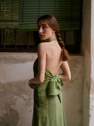 Woman wearing a green dress with a backless design, standing against a textured wall.