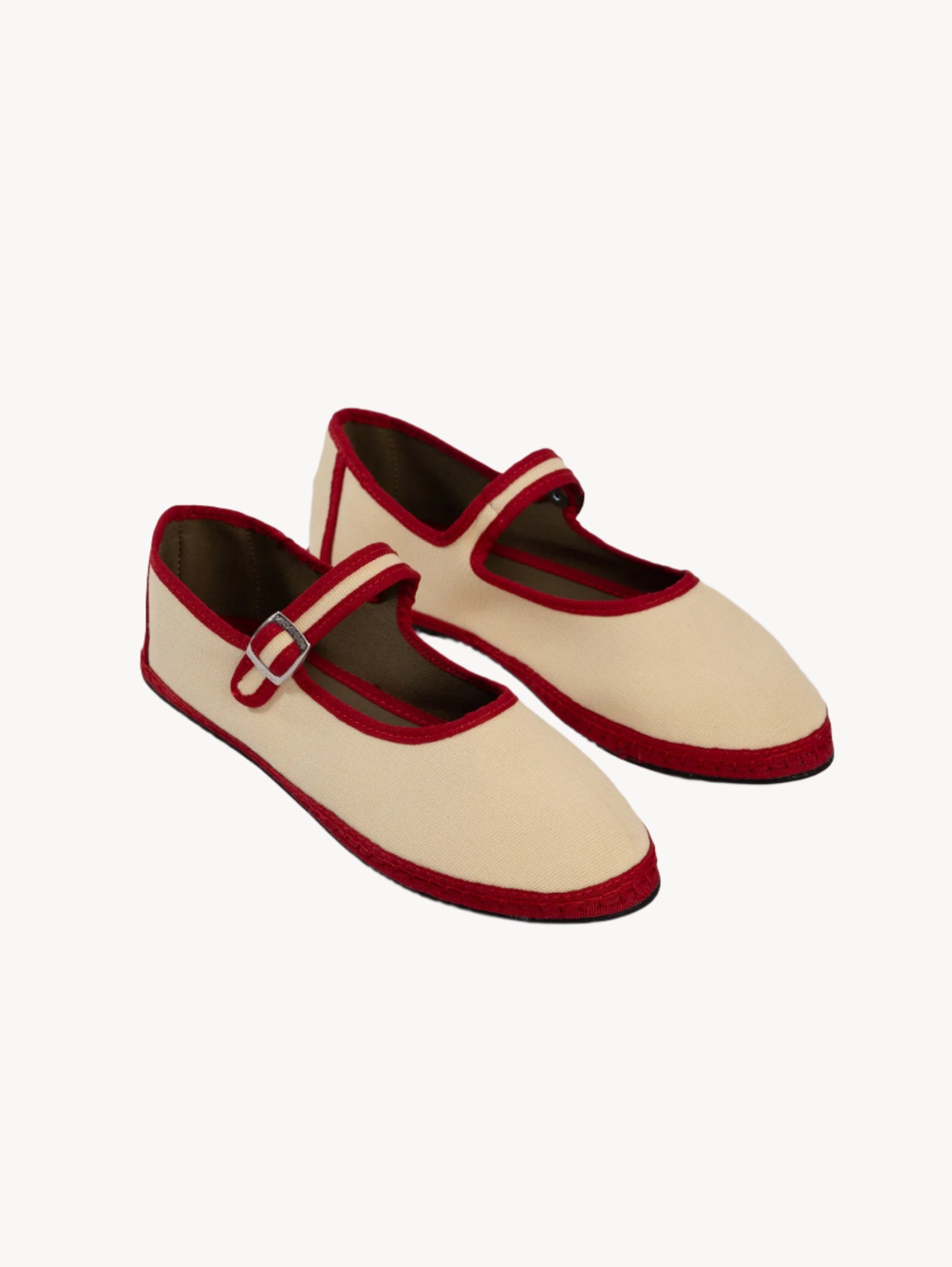 Pair of cream shoes with red accents on a light gray background
