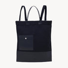 A black backpack with two handles, an interior pocket, and is made of a fabric that appears to be a blend of recycled plastic and vegetable tanning.